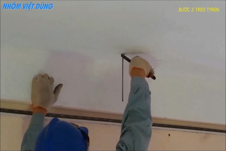 Người thợ đang cố định tyren với trần nhà bằng kìm và vít ở bước 3 trong cách thi công trần nhôm caro