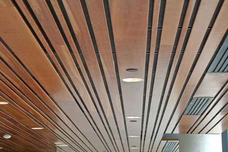 Trần nhôm giả gỗ B Multi-Shaped với màu vân gỗ nâu đỏ đậm kết hợp cùng đèn tròn chiếu sáng