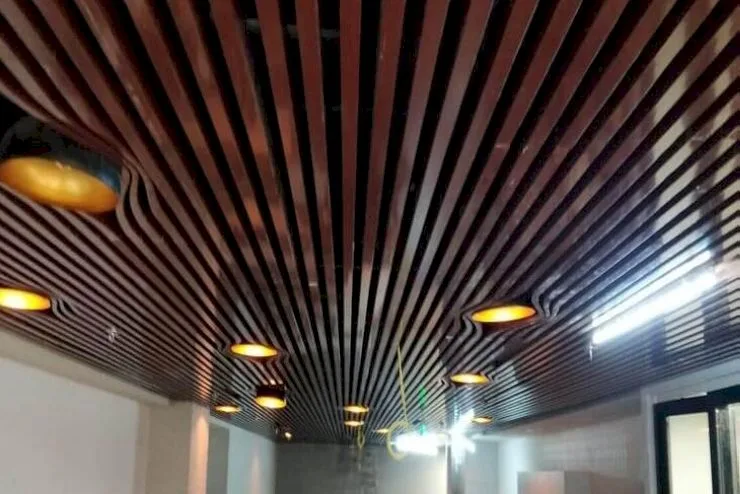 Tấm nhôm giả gỗ ốp trần kết hợp với hệ thống đèn trang trí màu vàng tạo nên hiệu ứng thị giác lạ mắt